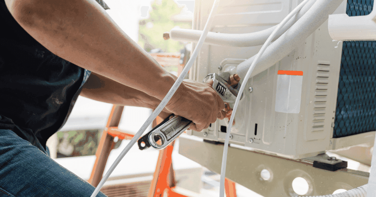 Technician tightening a refrigerant line fitting on an outdoor air conditioner unit with a wrench
