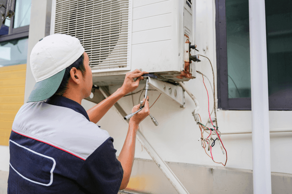 Technician working on the exposed wiring and refrigerant connections of an outdoor air conditioner unit