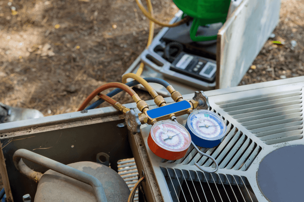 Pressure gauges and a digital scale connected to an open outdoor AC unit during a refrigerant recharge