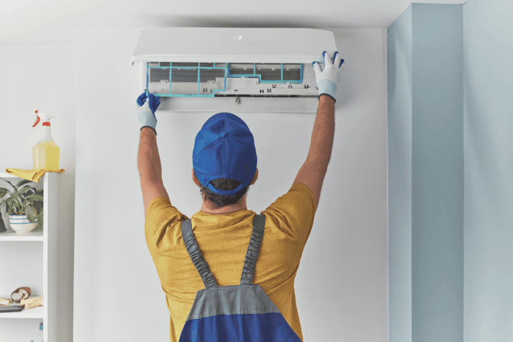 Technician removing the front filter panel of a wall-mounted split AC indoor unit for cleaning