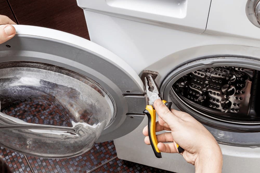 Hand using pliers on the door seal of a front-loading washing machine during a repair