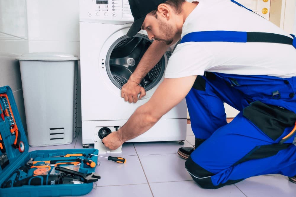 Technician kneeling with a tool belt, working on a washing machine during a repair