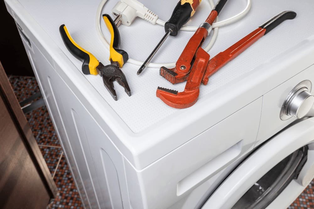 Hand tools — pliers, a pipe wrench and a screwdriver — laid out on top of a washing machine before a repair