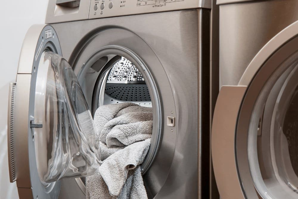 Open front-loading commercial tumble dryer with a towel spilling out of the drum
