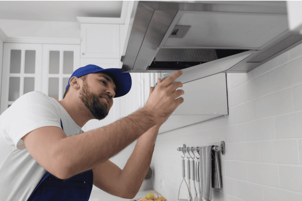 Technician in a blue cap adjusting a cooker hood above a kitchen counter
