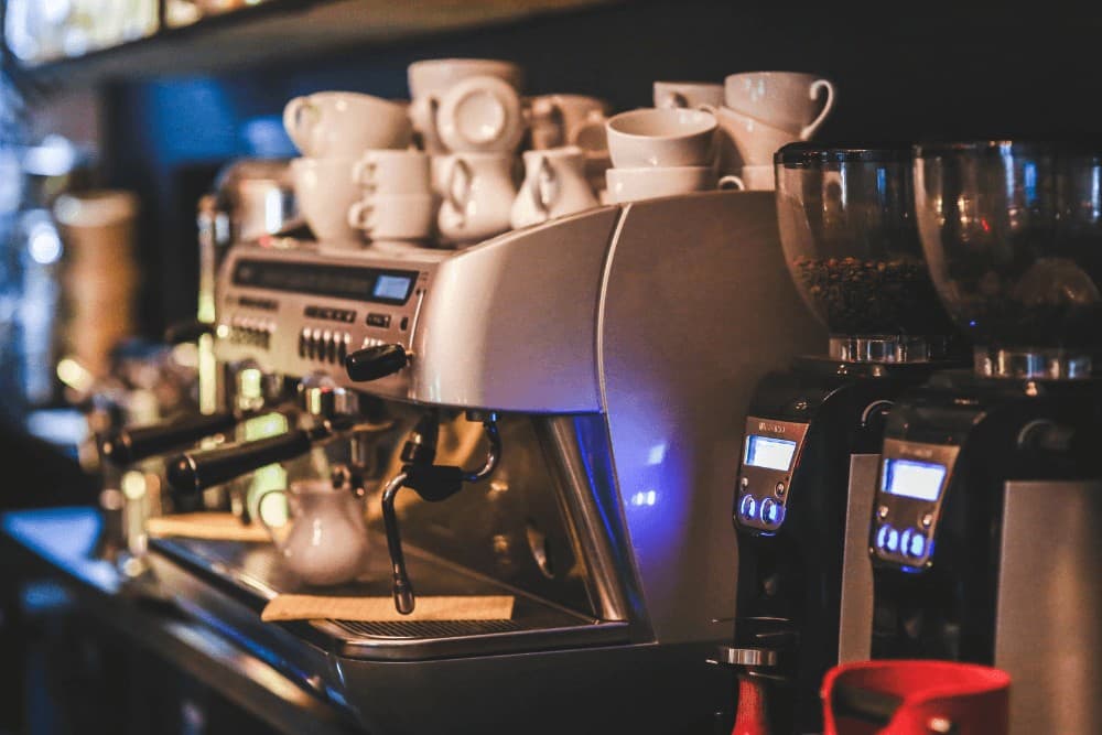 Professional espresso machine on a cafe counter with a row of cups, a coffee grinder and milk jugs arranged alongside it