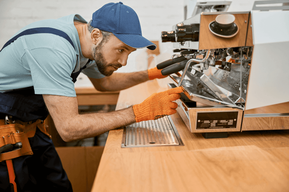 Technician in orange gloves servicing a commercial espresso machine on a café counter
