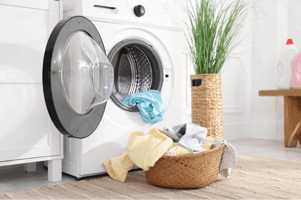 Front-loading washing machine with the door open and a basket of laundry on the floor