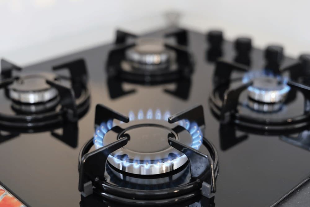 Close-up of a black glass gas hob with its burners lit, showing steady blue flames