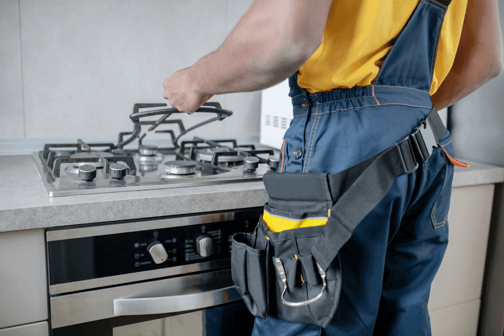 Technician with a tool belt adjusting the grate of a built-in gas hob above a built-in oven