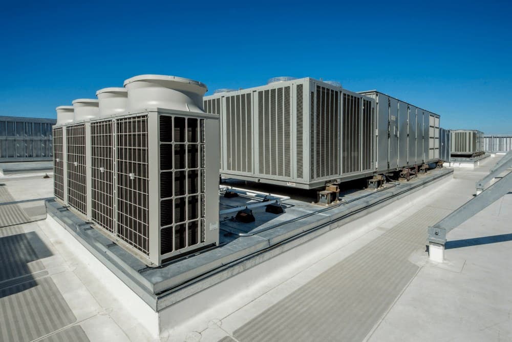 Large rooftop commercial air conditioning condenser and chiller units under a blue sky
