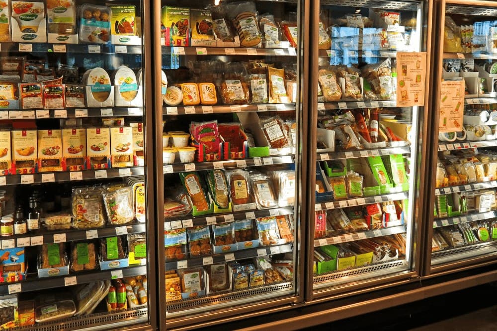 Row of glass-door commercial freezers stocked with frozen food in a supermarket aisle
