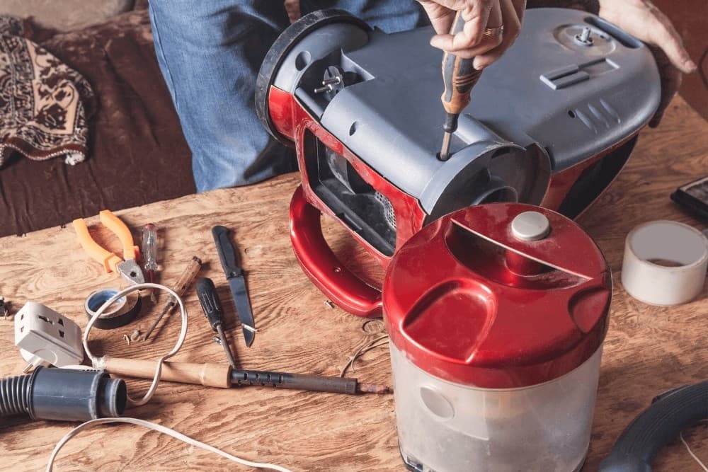Vacuum cleaner fully disassembled on a workbench — motor housing, cyclone unit and hose separated, with screwdrivers and other hand tools laid out beside the parts during a fault diagnosis