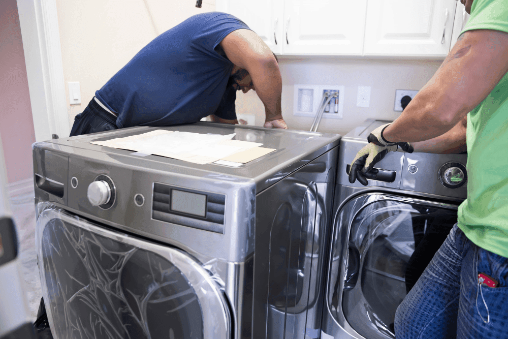 Two technicians installing a graphite front-loading washer and dryer pair in a laundry room