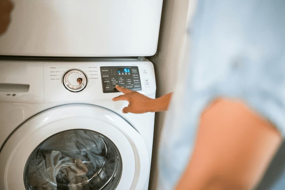 Close-up of a hand pressing a button on a washing machine's control panel during a function test after repair