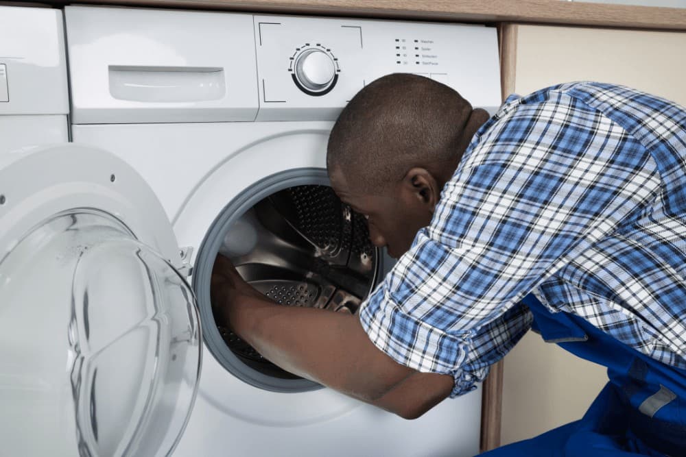 Technician in a plaid shirt reaching into the drum of an open front-loading washing machine to check it
